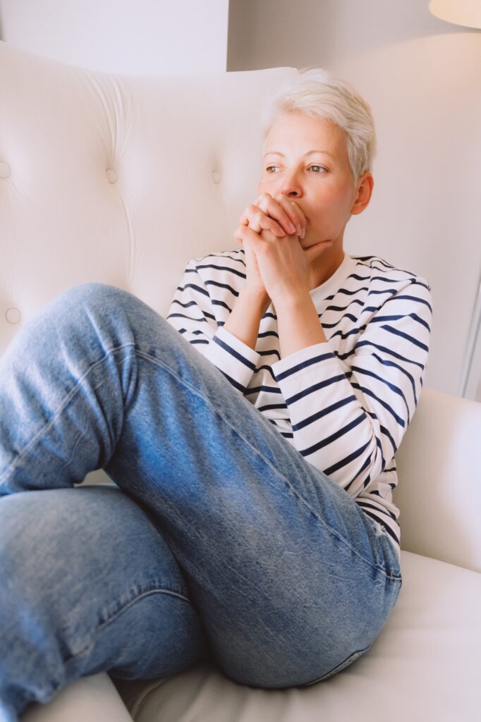 Unhappy middle age blonde woman stay at home, sitting in big white armchair alone, feeling lonely .